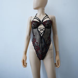 Puede incluir: Body de encaje negro con bordado floral rojo y un dise&ntilde;o de tirantes cruzados.