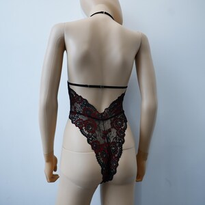 Puede incluir: Body de encaje negro con detalles florales rojos. El body tiene una correa de cuello halter y una espalda baja.
