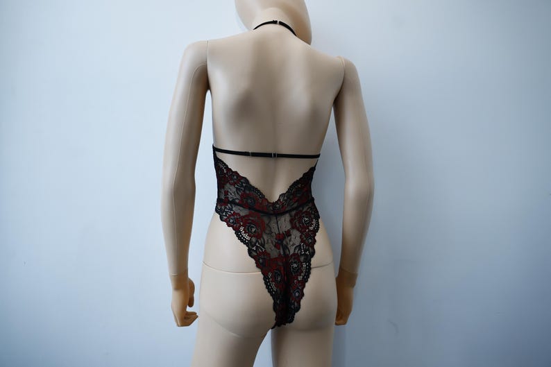 Puede incluir: Body de encaje negro con detalles florales rojos. El body tiene una correa de cuello halter y una espalda baja.
