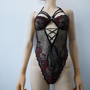 Puede incluir: Body de encaje negro con bordado floral rojo y dise&ntilde;o de tirantes cruzados.