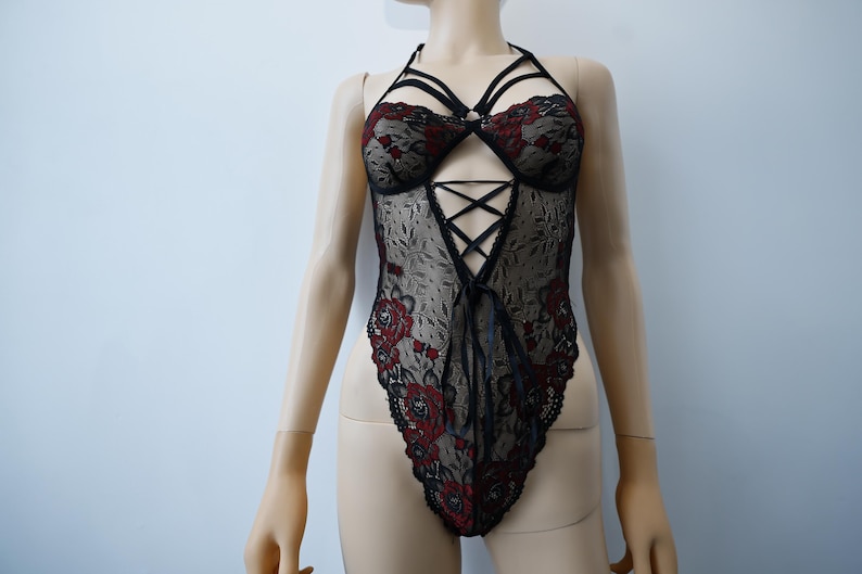 Puede incluir: Body de encaje negro con bordado floral rojo y dise&ntilde;o de tirantes cruzados.