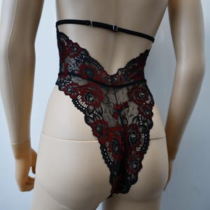 Puede incluir: Body de encaje negro con bordado floral rojo. El body tiene la espalda baja y tirantes ajustables.