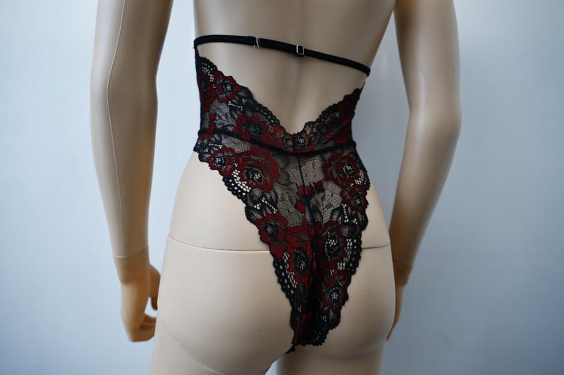 Puede incluir: Body de encaje negro con bordado floral rojo. El body tiene la espalda baja y tirantes ajustables.