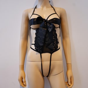 Puede incluir: Lencería negra de encaje con un gran lazo negro en el pecho.