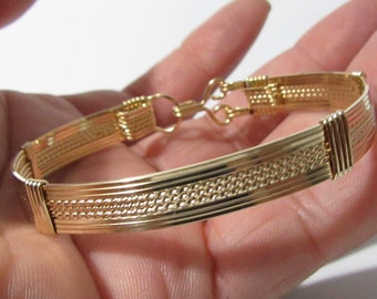 Könnte beinhalten: Ein goldfarbenes Drahtarmband mit gewebtem Muster. Das Armband hat einen Verschluss.