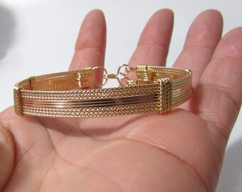 Könnte beinhalten: Ein goldfarbenes Drahtarmband mit geflochtenem Design. Das Armband hat einen Verschluss.