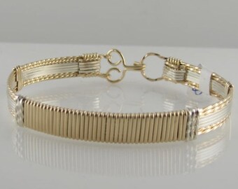 Könnte beinhalten: Ein Armband aus Gold- und Silberdraht mit geflochtenem Design. Das Armband hat einen Verschluss.