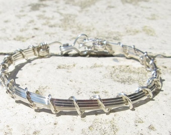 May include: A silver wire wrapped bangle bracelet. The bracelet is made of multiple strands of wire that are twisted together to create a unique and textured design.
