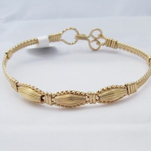 May include: A gold wire bracelet with a twisted wire design and three oval-shaped accents. The bracelet has a clasp closure.