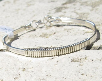 May include: A silver wire wrapped bracelet with a clasp closure. The bracelet is made of multiple strands of wire that are woven together to create a textured look.