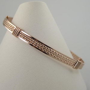 Puede incluir: Un brazalete de alambre envuelto en oro rosa con un diseño texturizado.