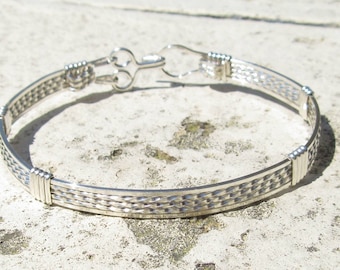 May include: A silver bracelet with a woven design and a clasp closure.
