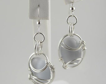 May include: Silver dangle earrings with a light grey oval-shaped stone wrapped in silver wire.