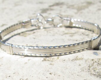 May include: A silver bangle bracelet with a braided design and a clasp closure.