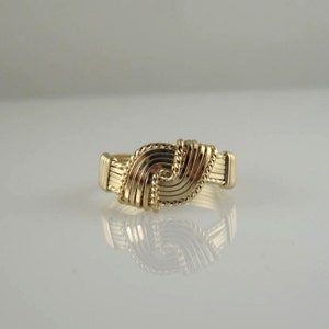 May include: A gold ring with a woven design. The ring is made of multiple strands of wire that are woven together to create a knot-like pattern.