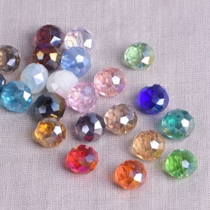 May include: A collection of faceted, round beads in various colors, including red, orange, yellow, green, blue, and purple. The beads have a shiny, iridescent finish and are scattered on a light gray fabric surface.