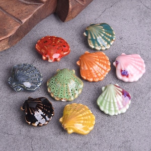 Può includere: Assortimento di nove conchiglie in ceramica di vari colori e motivi, tra cui verde, blu, arancione, rosa, giallo e nero.
