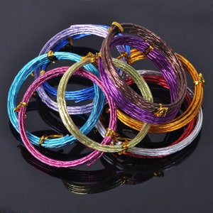 May include: A collection of colorful, metallic wire coils in shades of blue, purple, pink, gold, and silver. Each coil is bound with a small gold-colored clasp. The wires are arranged in a circular pattern, creating a visually appealing display.