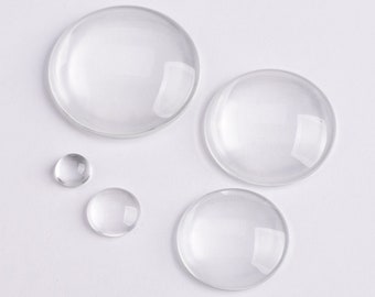 May include: Four clear glass cabochons of varying sizes. The largest cabochon is approximately 2 inches in diameter, while the smallest is about 1/2 inch in diameter.