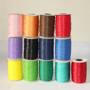 Può includere: Una collezione di bobine di cordoncino cerato in vari colori, tra cui rosa, arancio, marrone, rosso, viola, nero, blu, giallo, verde, turchese e rosso. Le bobine sono disposte su due file.