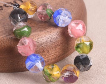 May include: A strand of faceted beads in various colors, including pink, blue, yellow, green, and black. The beads are strung together on a clear cord, and are displayed on a wooden surface. The beads have a geometric shape.