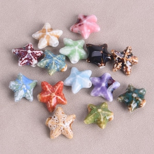Op de afbeelding: Assortiment van keramische zeesterren kralen in verschillende kleuren en patronen, waaronder blauw, groen, rood, paars en bruin. De kralen zijn perfect voor het maken van sieraden, knutselen en decoratie.
