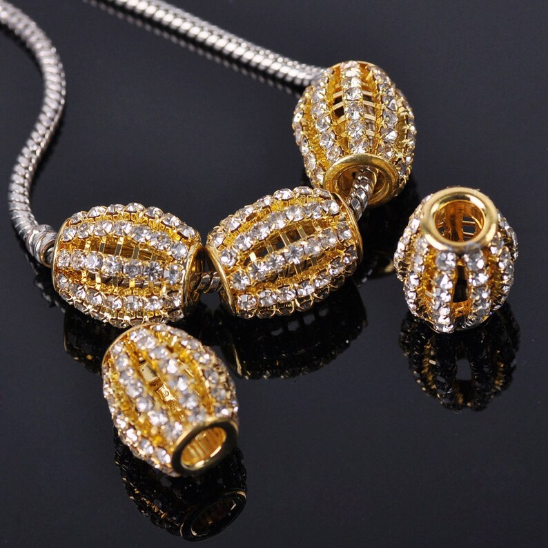 May include: A gold chain necklace with four gold and clear crystal bead charms. The beads are oval shaped and have a geometric design.