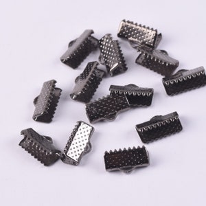 May include: A group of 15 black metal clasps for jewelry making. The clasps are rectangular with a textured surface and a small loop on one side.