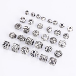 May include: Assortment of silver metal beads with various designs and shapes, including round, square, and cylindrical beads.