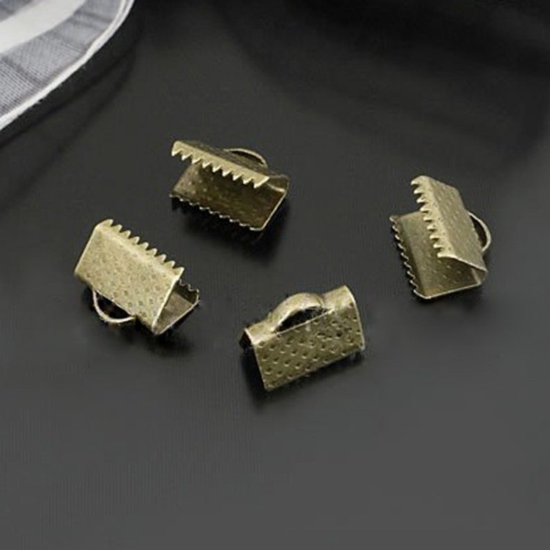 May include: Four antique gold metal cord end stoppers. The stoppers have a textured surface and a small loop on one side.