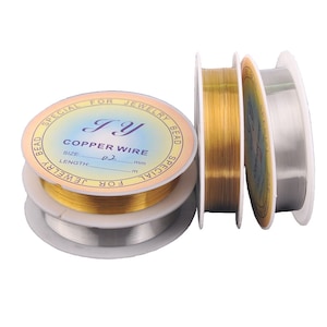 Op de afbeelding: Drie spoelen koperdraad voor het maken van sieraden. De spoelen zijn gelabeld met "JY Copper Wire" met de maat 0,2 mm. De draad is goudkleurig.