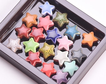 May include: A collection of ceramic star-shaped beads in a variety of colors, including blue, green, red, orange, yellow, and purple. The beads are arranged in a brown tray.