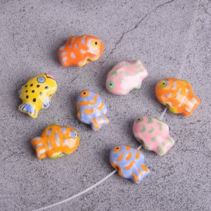 May include: A set of eight ceramic fish beads in various colors, including yellow, orange, blue, pink, and green. The beads are painted with stripes and spots and have a glossy finish.