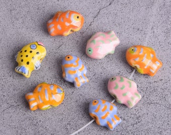 May include: A set of eight ceramic fish beads in various colors, including yellow, orange, blue, pink, and green. The beads are painted with stripes and spots and have a glossy finish.