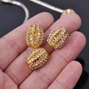 May include: Three gold-toned barrel-shaped beads with clear rhinestone accents. The beads are approximately 1 inch in length and have a decorative, cage-like design.