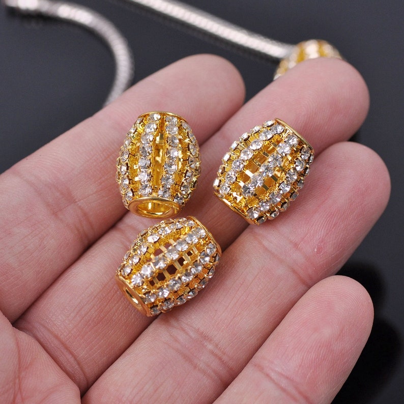 May include: Three gold-toned barrel-shaped beads with clear rhinestone accents. The beads are approximately 1 inch in length and have a decorative, cage-like design.