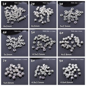 May include: Nine different sizes of silver metal beads with a decorative design. The beads are arranged in rows with the size and hole size listed below each row.