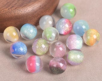 May include: A collection of round, translucent beads featuring multi-colored gradients and embedded glitter particles. Each bead has a central hole for threading, with various color combinations including pink, blue, yellow, green, and purple hues.