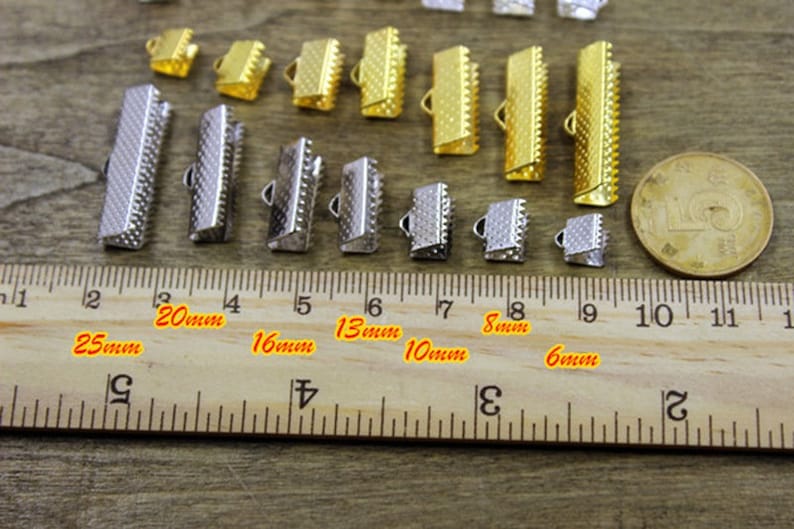 May include: Assortment of gold and silver metal clasps in various sizes, measured in millimeters, for jewelry making. The clasps are arranged on a wooden ruler.