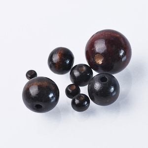 Può includere: Un gruppo di perline di legno di diverse dimensioni e tonalità di marrone. Le perline sono rotonde e hanno una finitura liscia e lucida.