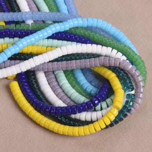 May include: A selection of colourful, spiral-shaped glass beads in shades of blue, green, yellow, white, and purple. The beads are arranged in a layered, intertwined pattern, highlighting their glossy texture and vibrant hues. Suitable for jewellery making.