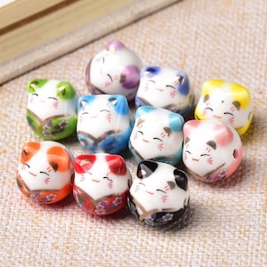 May include: Ten ceramic cat figurines with different colored glazes. Each figurine has a white face with black eyes and a pink nose. The figurines are all in a sitting position with their paws tucked under them.