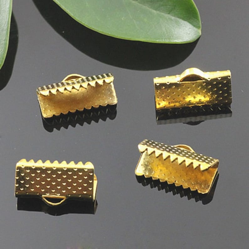 May include: Four gold-colored metal clasps for jewelry making. Each clasp has a textured surface and a scalloped edge.