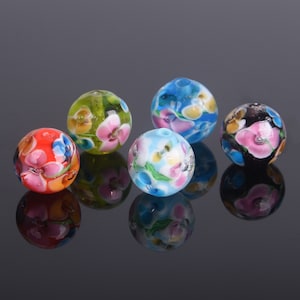 May include: Five round glass beads with floral patterns. The beads are in various colors, including green, blue, red, black, and white.