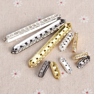 May include: Assortment of silver and gold-toned metal embellishments with clear rhinestones. The embellishments are in various shapes and sizes, including rectangular, oval, and round.