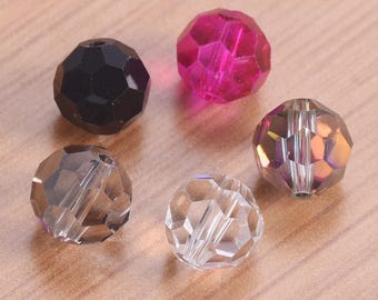 May include: Five faceted beads in various colors: black, clear, pink, and iridescent. Each bead has a hole for stringing. The beads are arranged on a light brown surface, suitable for jewelry making or crafts.