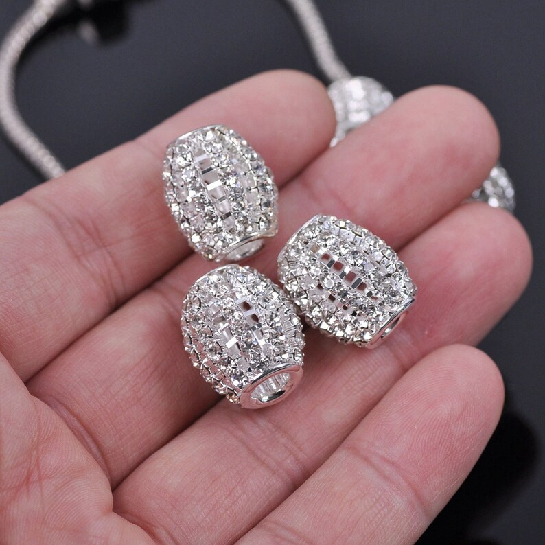 May include: Three silver-toned, oval-shaped beads with clear rhinestones covering the entire surface.