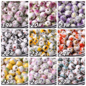 May include: Nine different styles of ceramic beads with various floral and abstract designs. The beads are white with colorful floral patterns. The beads are numbered 19 through 27.