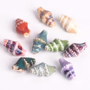 May include: Assortment of ten ceramic seashell beads in various colours, including pink, green, blue, purple, and brown. Each bead has a spiral design and white accents.