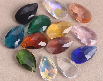 May include: A collection of faceted teardrop-shaped crystal beads in various colors, including black, green, yellow, orange, pink, and blue. The beads have a hole at the top for stringing and are arranged on a neutral surface.